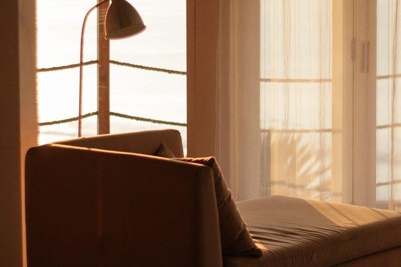 A low upholstered seat in a warm room with evening light through the glass doors